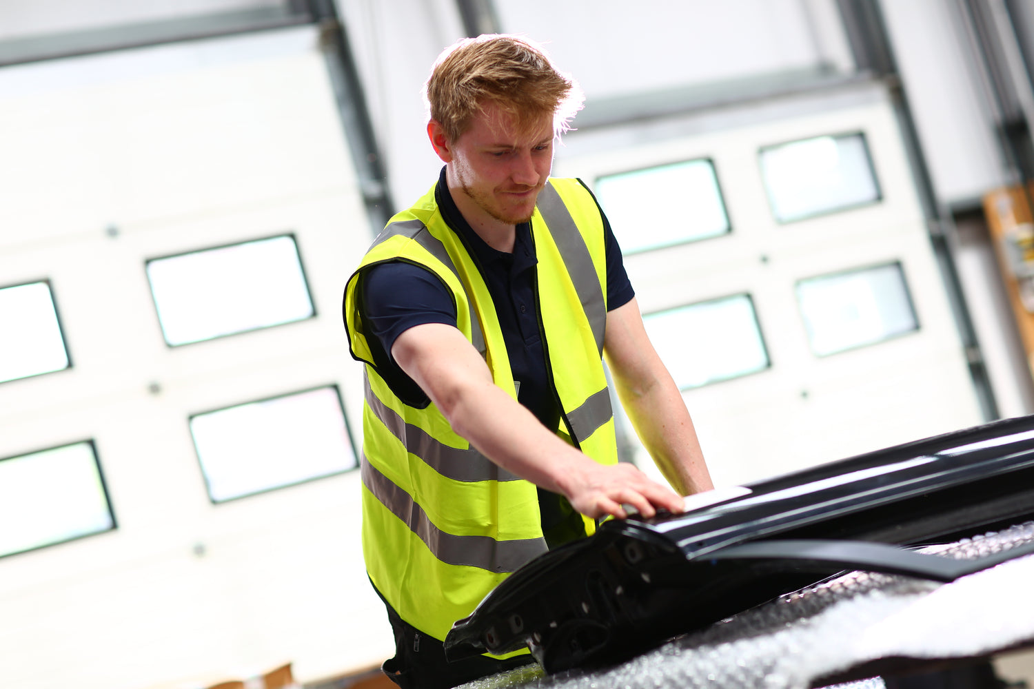 Person in a high-visibility vest working on a car in an indoor setting