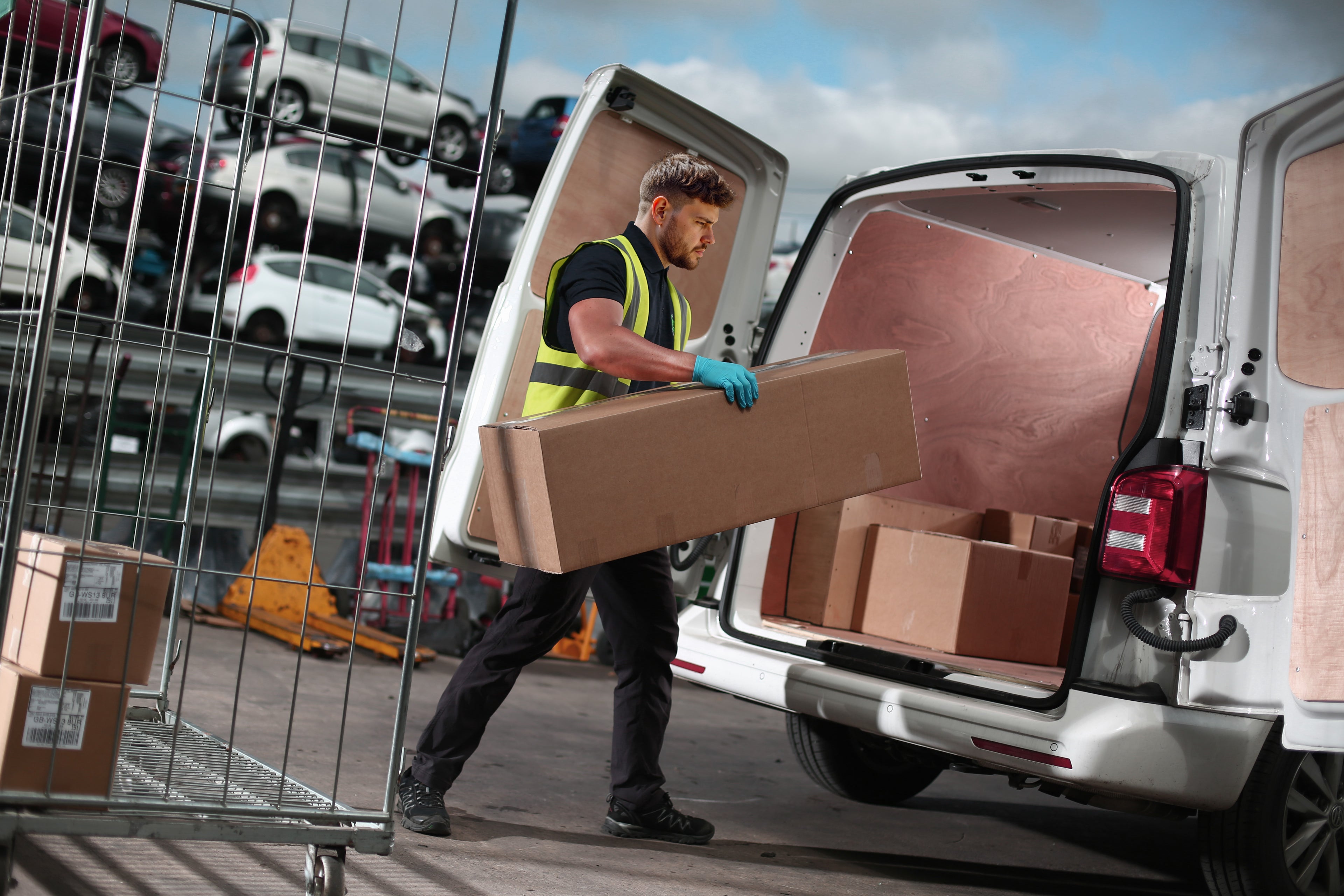 Man loading boxes into a van with a car scrapyard in the background