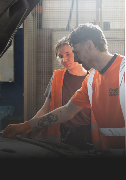 Two people in high-visibility vests working on a car in a garage.