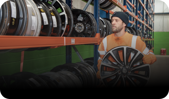 Man in a warehouse with shelves of tires and a large tire in front of him.